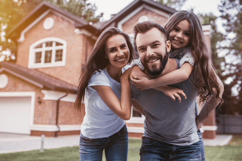 Family of 3 smiling in front of home